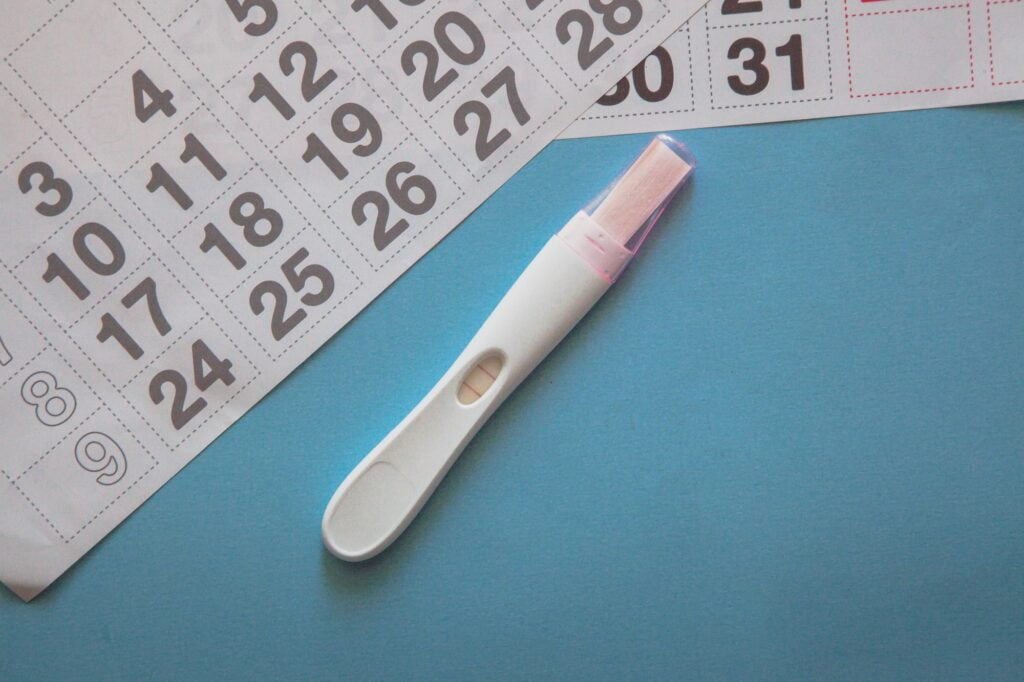 Positive pregnancy test and a calendar on the blue background. Pregnancy concept. Dye Stealer Pregnancy Test