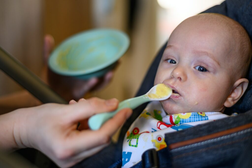 Adorable cute baby eating baby food while mom feeds him